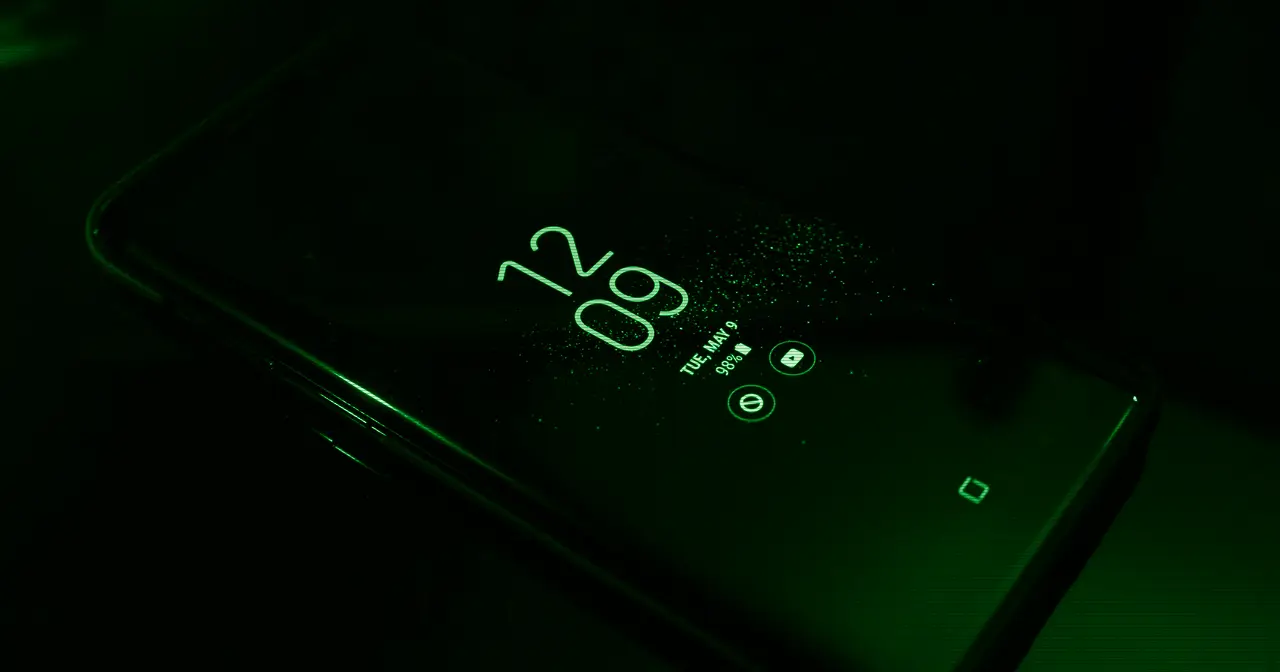 Pantalla de un smartphone encendido en la oscuridad con el reloj y las notificaciones, que ilustra la interfaz Liquid Glass de OriginOS 7
